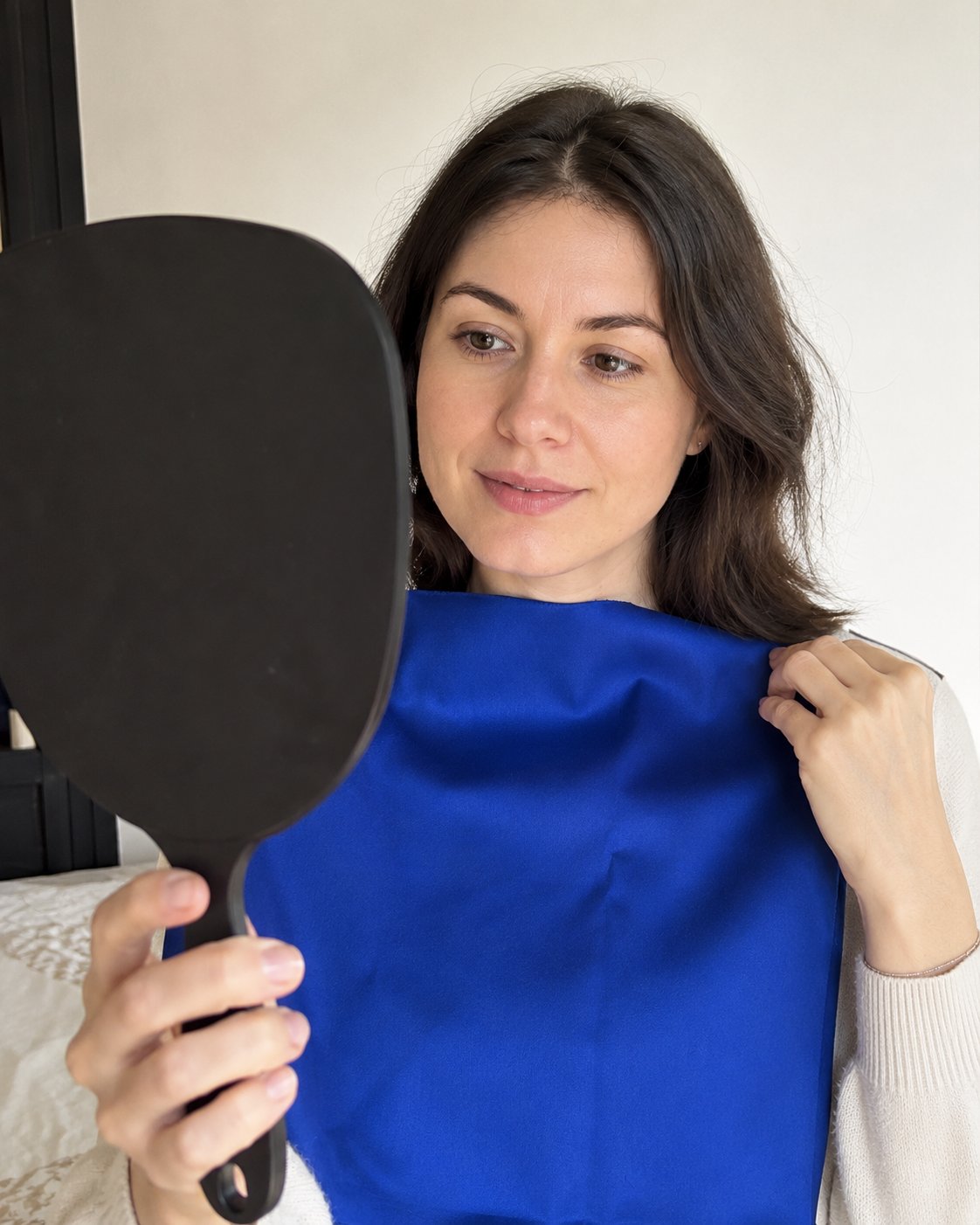 Frau hält ein königsblaues Tuch nahe am Gesicht und schaut in einen Handspiegel, Farb-Draping-Test
